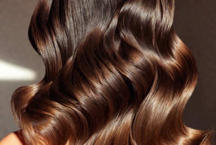 Rich Girl Blowout 2026 — The Luxury Hair Trend Replacing Beach Waves Cinematic close-up of sleek voluminous high-shine blowout hair in warm studio lighting representing the rich girl blowout luxury hair trend replacing beach waves in 2026