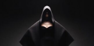 Balenciaga’s Architectural Runway Show Sparks Debate Over the Future of Luxury Fashion Model in dramatic oversized cocooning coat on a pitch-black runway with chiaroscuro spotlight lighting representing the Balenciaga runway 2026 ClairObscur collection by Pierpaolo Piccioli at Paris Fashion Week