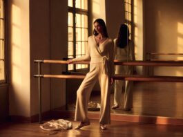 Model in wrap cardigan and satin ballet flats at a barre in a sunlit studio representing how the balletcore trend 2026 is inspiring adult ballet enrollment and luxury fashion