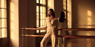 Model in wrap cardigan and satin ballet flats at a barre in a sunlit studio representing how the balletcore trend 2026 is inspiring adult ballet enrollment and luxury fashion