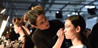Beauty Trends Hub: Runway Makeup, Hair & Skincare from Fashion Week Makeup artist applying editorial runway beauty look to a model backstage at a fashion week show, representing the Beauty Trends Hub covering runway makeup, hair, and skincare trends