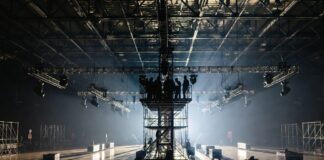 Production crew setting up lighting rigs and staging inside a fashion week show venue, representing the behind the scenes costs of runway show production