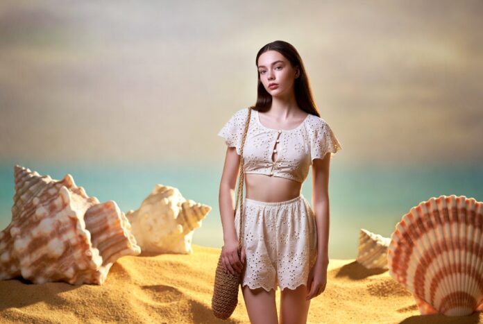 Young woman in ivory eyelet ensemble on a dreamlike beach representing the Apple Martin Chloé campaign and the celebrity children fashion debate in luxury advertising 2026