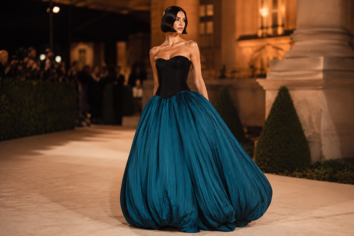 Chrissy Teigen Bubble Skirt Dress — Gold Gala 2026 Chrissy Teigen wearing a strapless black corseted bodice and dramatic teal bubble skirt by Aisté Hong at the 2026 Gold Gala red carpet.