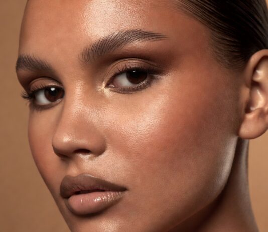 Latte Makeup Is Still Dominating—How Warm Bronze Tones Became 2026’s Most Wearable Glam Look Model wearing a latte makeup look with warm bronze eye shadow, cream bronzer on sun-kissed cheekbones, and a nude glossy lip against a warm champagne editorial background — illustrating the 2026 bronze makeup trend.