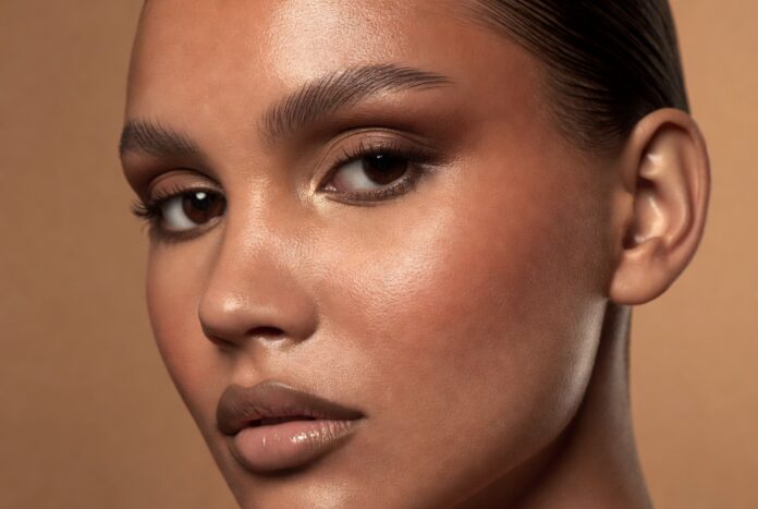 Latte Makeup Look 2026 — Warm Bronze Glam Model wearing a latte makeup look with warm bronze eye shadow, cream bronzer on sun-kissed cheekbones, and a nude glossy lip against a warm champagne editorial background — illustrating the 2026 bronze makeup trend.