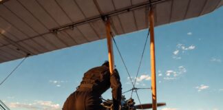 Cinematic shot of a figure gripping a biplane wing above a canyon at golden hour representing Tom Cruise's record-breaking stunts in Mission Impossible Final Reckoning