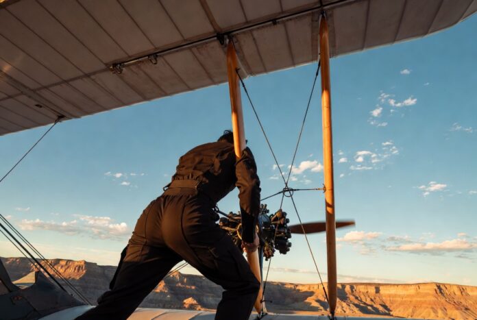 Cinematic shot of a figure gripping a biplane wing above a canyon at golden hour representing Tom Cruise's record-breaking stunts in Mission Impossible Final Reckoning