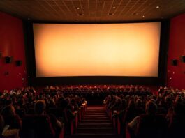 Wide shot of a packed premium movie theater auditorium with glowing screen light representing summer movies 2026 and Hollywood's biggest box office comeback season since the pandemic