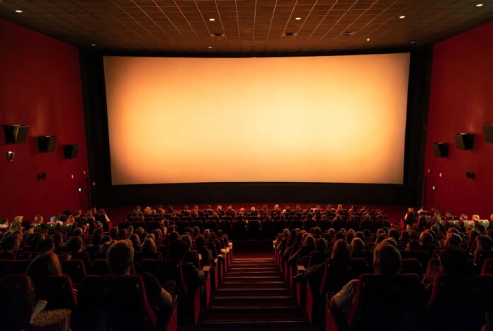 Summer Movies 2026 — Hollywood's Biggest Comeback Season Wide shot of a packed premium movie theater auditorium with glowing screen light representing summer movies 2026 and Hollywood's biggest box office comeback season since the pandemic