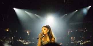 A glamorous pop superstar performing on a brightly lit arena stage with a microphone, evoking a major comeback tour