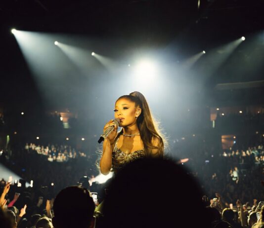 A glamorous pop superstar performing on a brightly lit arena stage with a microphone, evoking a major comeback tour