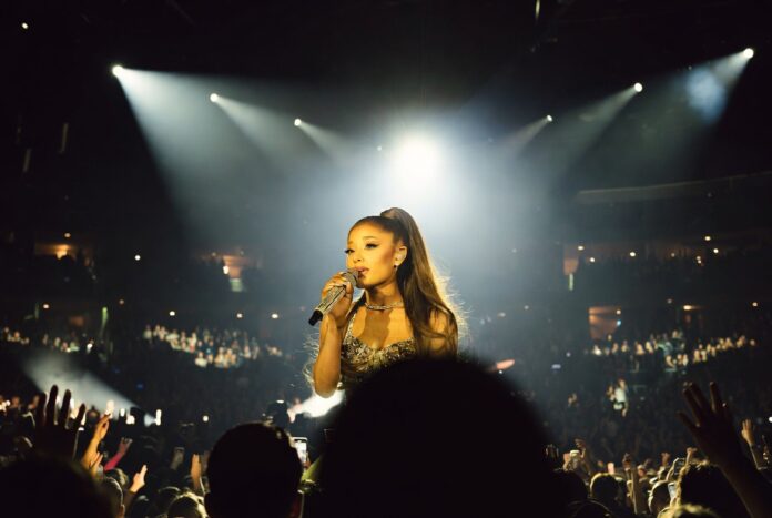 Ariana Grande New Music Streaming Billboard 2026 A glamorous pop superstar performing on a brightly lit arena stage with a microphone, evoking a major comeback tour