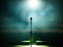 A moody, atmospheric concert stage bathed in green and blue light evoking a Gen Z alternative pop superstar