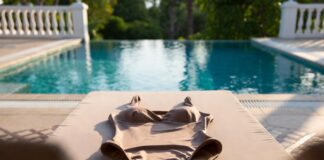 Celebrity-Loved Swimwear Brands Are Driving Luxury Swimsuit Sales Luxury one-piece swimsuit displayed on a poolside lounger at a high-end resort in soft afternoon light.