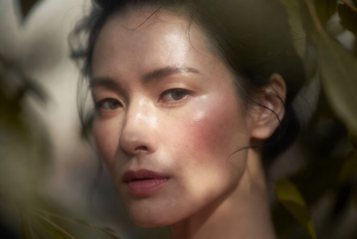 Close-up of a woman with glowing dewy natural skin and barely-there makeup in soft diffused light.