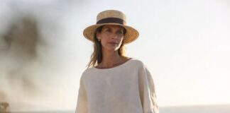A woman in a relaxed linen outfit with neutral tones and a straw hat by the sea in soft summer light