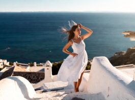 Woman in a white linen dress standing on whitewashed Mediterranean steps with blue sea views.