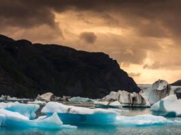 Sweeping Arctic landscape with icebergs floating in a fjord under a dramatic summer sky.