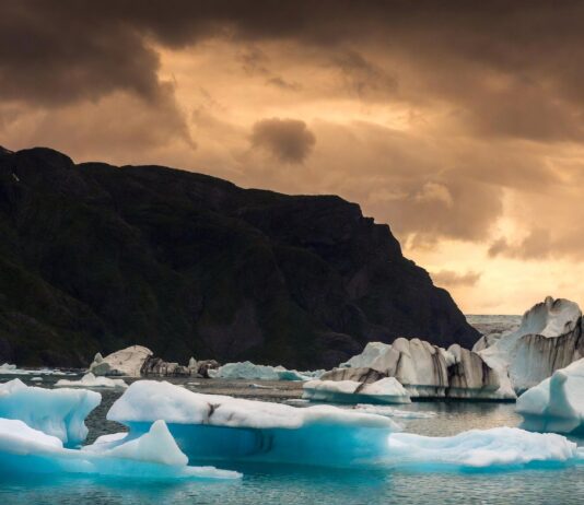The ‘Coolcation’ Trend Is Exploding – Travelers Are Choosing Cooler Destinations Instead of Heat Waves Sweeping Arctic landscape with icebergs floating in a fjord under a dramatic summer sky.