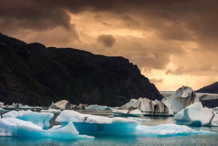 Sweeping Arctic landscape with icebergs floating in a fjord under a dramatic summer sky.