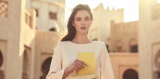 A model in soft cream resort tailoring holding a structured top-handle bag in warm summer light