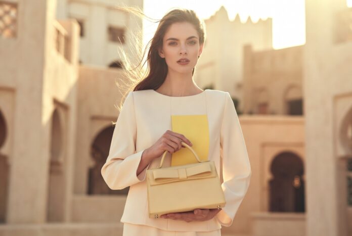 Dior Cruise 2026 Summer Resort Glamour Style A model in soft cream resort tailoring holding a structured top-handle bag in warm summer light