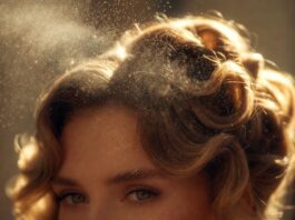 A fine mist of luxury hair perfume being spritzed onto glossy, glamorous honey-blonde waves in soft light