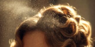A fine mist of luxury hair perfume being spritzed onto glossy, glamorous honey-blonde waves in soft light