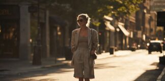 A woman wearing tailored knee-length Bermuda shorts with an oversized blazer and minimal sandals in summer street style