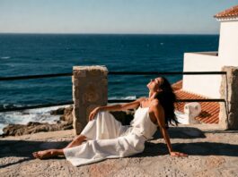 Matching Linen Sets Are Becoming the Ultimate Vacation Wardrobe Essential Woman in a white wide-leg linen set on a sun-drenched European terrace overlooking a blue sea.