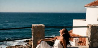 Woman in a white wide-leg linen set on a sun-drenched European terrace overlooking a blue sea.