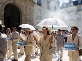 Elegant fashion week guests shielding from intense Paris heat outside a luxury runway venue