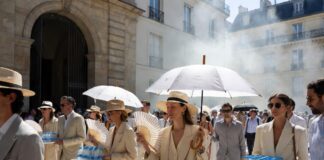 Elegant fashion week guests shielding from intense Paris heat outside a luxury runway venue