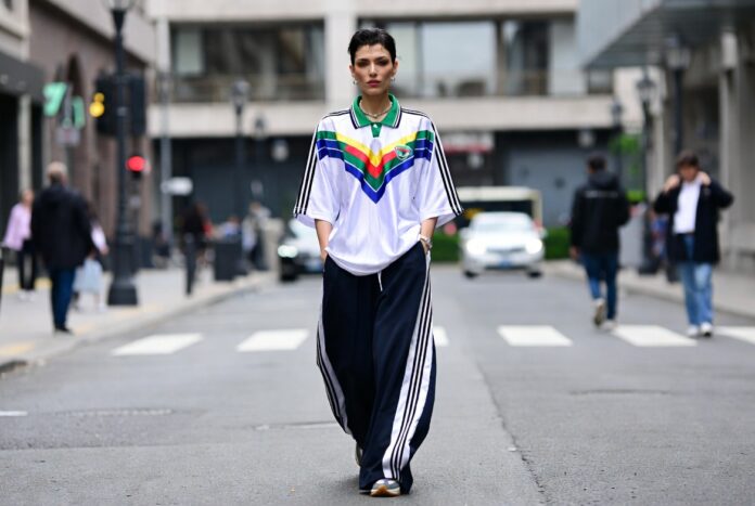 Fashion week attendee in a vintage soccer jersey and wide-leg track pants walking on a city street.