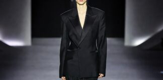 Model in a sharp oversized black tuxedo blazer on a sleek Paris runway with dramatic lighting.