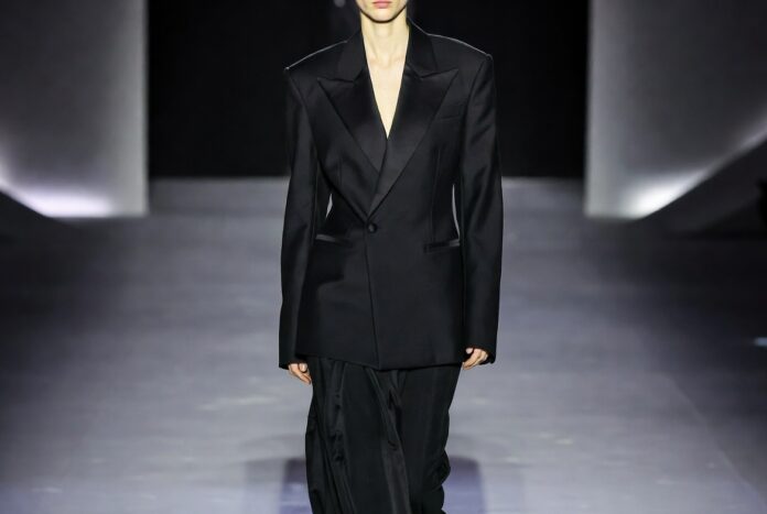 Saint Laurent Fall 2026 Tailoring Power Dressing Model in a sharp oversized black tuxedo blazer on a sleek Paris runway with dramatic lighting.