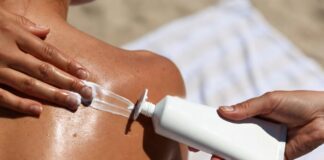 Sunscreen being applied to bare shoulders in bright summer sunlight, with a tube of SPF visible beside.