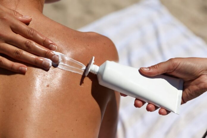Summer Sunscreen Tips SPF Skincare Routine 2026 Sunscreen being applied to bare shoulders in bright summer sunlight, with a tube of SPF visible beside.