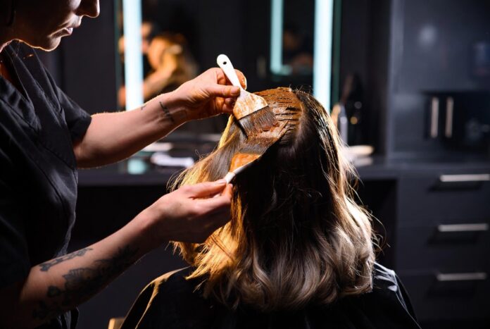 Colorist applying rich warm hair color to a client in a luxury salon representing the celebrity colorist as brand phenomenon in 2026 and the rise of Tracey Cunningham Chris McMillan and Chase Kusero as hair industry beauty influencers