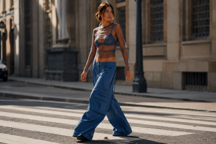 Woman in ocean-blue wide-leg cargo pants and a sheer layered top walking on a sunlit city street.