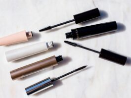 Viral TikTok Mascaras Are Replacing Luxury Lash Products in 2026 Editorial beauty flatlay of mascara tubes and open wands arranged on white marble representing the best mascara 2026 comparison between viral TikTok drugstore formulas and luxury clean beauty brands