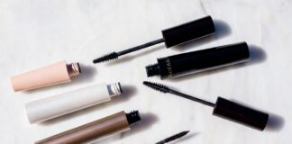 Viral TikTok Mascaras Are Replacing Luxury Lash Products in 2026 Editorial beauty flatlay of mascara tubes and open wands arranged on white marble representing the best mascara 2026 comparison between viral TikTok drugstore formulas and luxury clean beauty brands