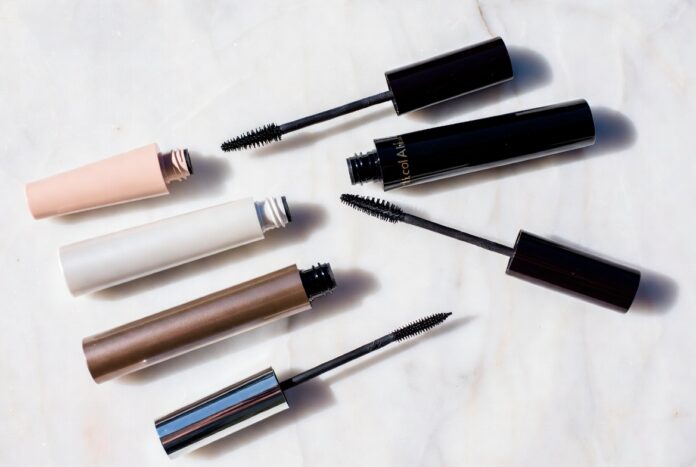 Editorial beauty flatlay of mascara tubes and open wands arranged on white marble representing the best mascara 2026 comparison between viral TikTok drugstore formulas and luxury clean beauty brands