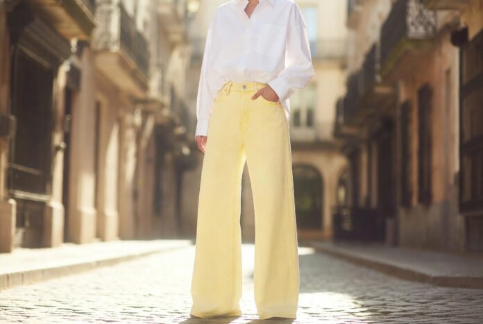 Fashion figure in butter yellow wide-leg pastel denim jeans with white oversized shirt on sunlit European street representing the pastel denim trend 2026 and the shift from indigo to soft pastel shades in summer street style