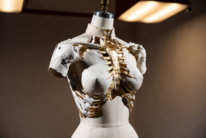 Three-dimensional gold torso couture piece on a dress form representing Schiaparelli anatomical fashion and the house's body-as-canvas design philosophy as explained by Runway Magazine