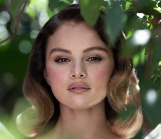 Selena Gomez’s Romantic Rare Beauty Campaign Is Fueling the Fairy Makeup Movement Woman in white tulle dress in a lush garden with rosy pink blush shimmering eyeshadow ultra-glossy lips and soft waves representing the Selena Gomez Rare Beauty fairy makeup aesthetic and garden photoshoot beauty look from the June 2026 campaign