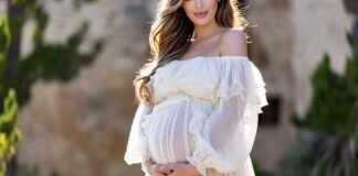 Anne Hathaway The Odyssey Look: A Romantic Blumarine Maternity Moment A pregnant woman cradling her baby bump in a flowing white ruffled boho maternity dress in summer