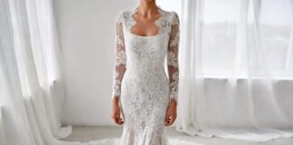 An elegant white lace column wedding gown with sheer sleeves and a long train in a bright bridal setting