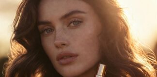 A model with glossy softly waved hair holds Fable & Mane styling oil in warm golden-hour light.